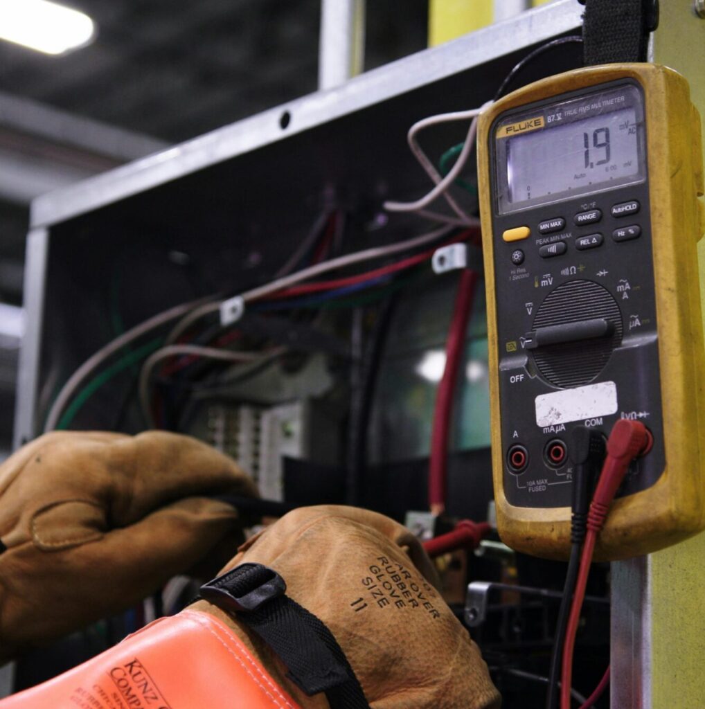 Electrician using a multimeter to fix industrial control panel wiring.