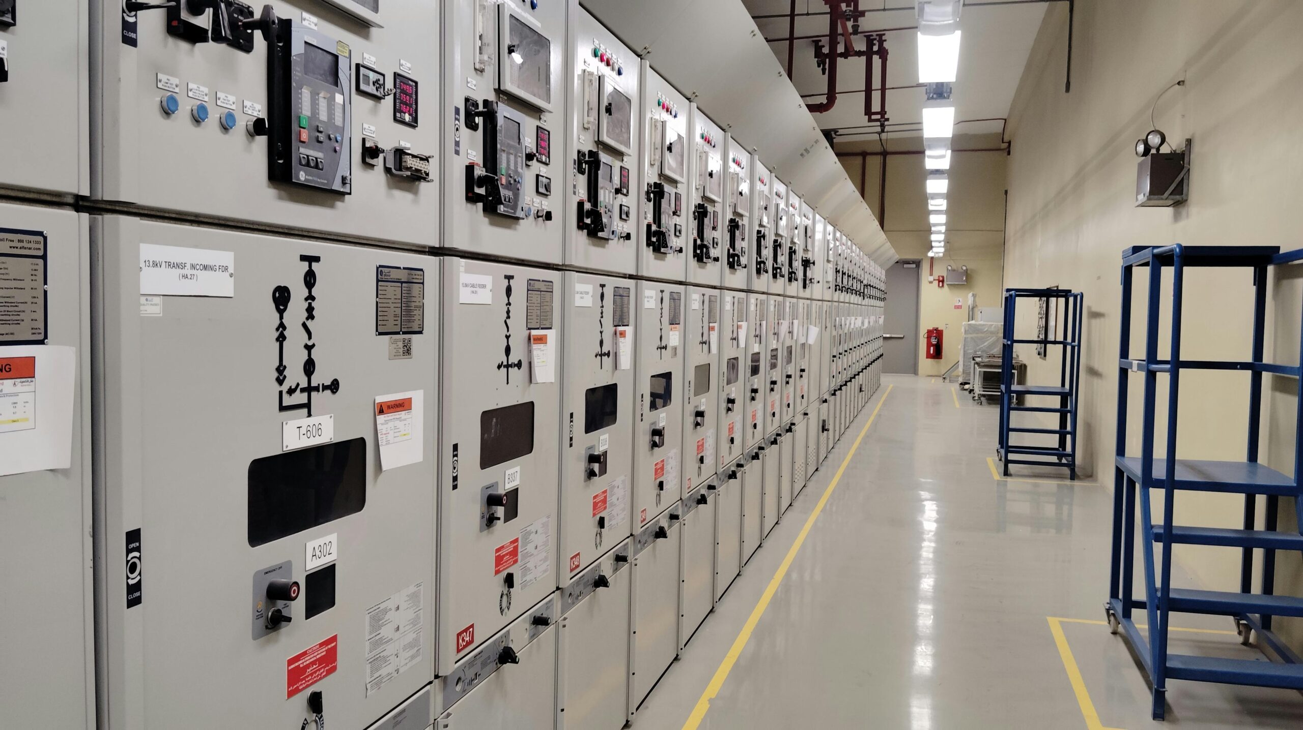 Long row of control panels in an industrial electrical control room, well-lit and spacious.